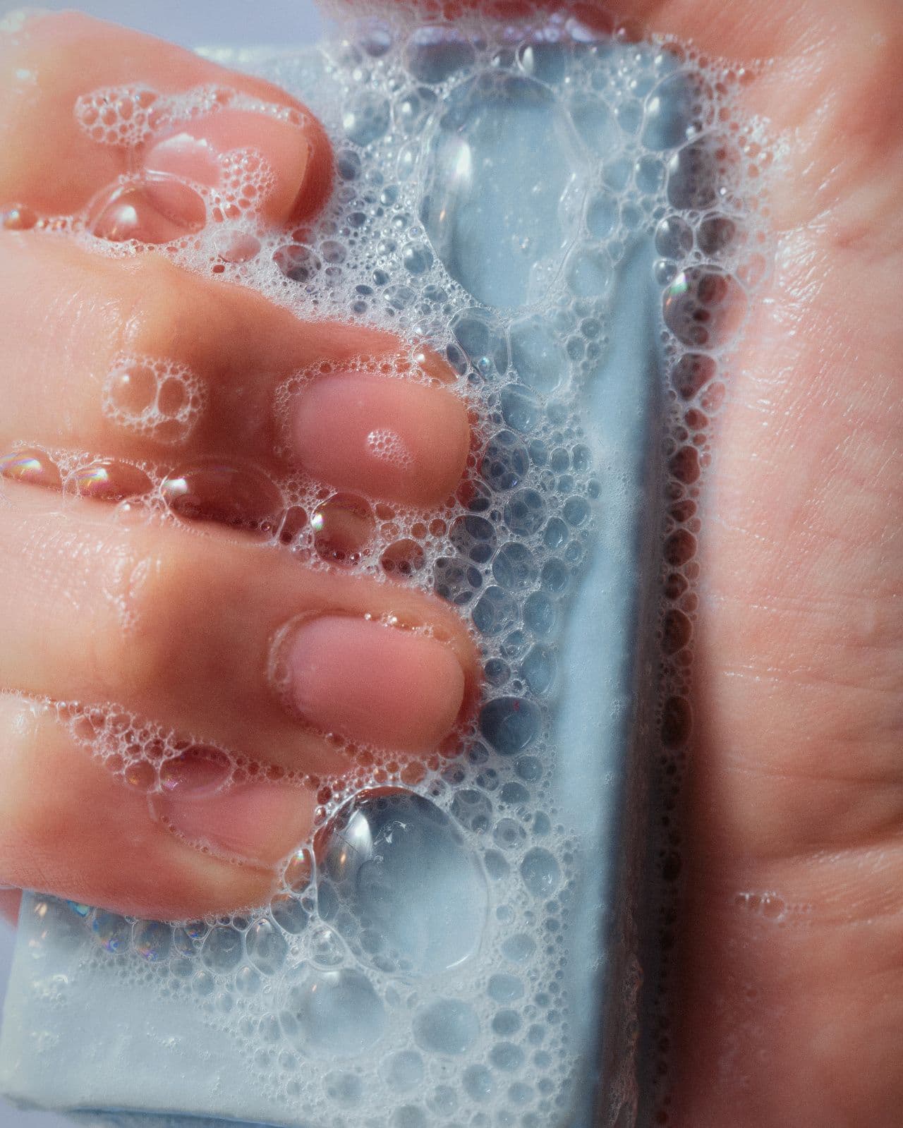 Hands lathering a pale blue bar of soap in dense foam