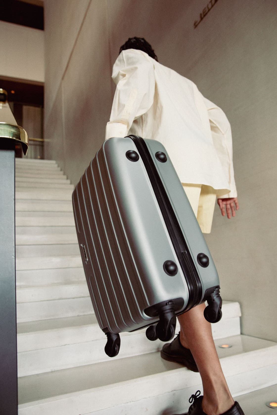 Hotel guest carrying a suitcase up a lobby staircase