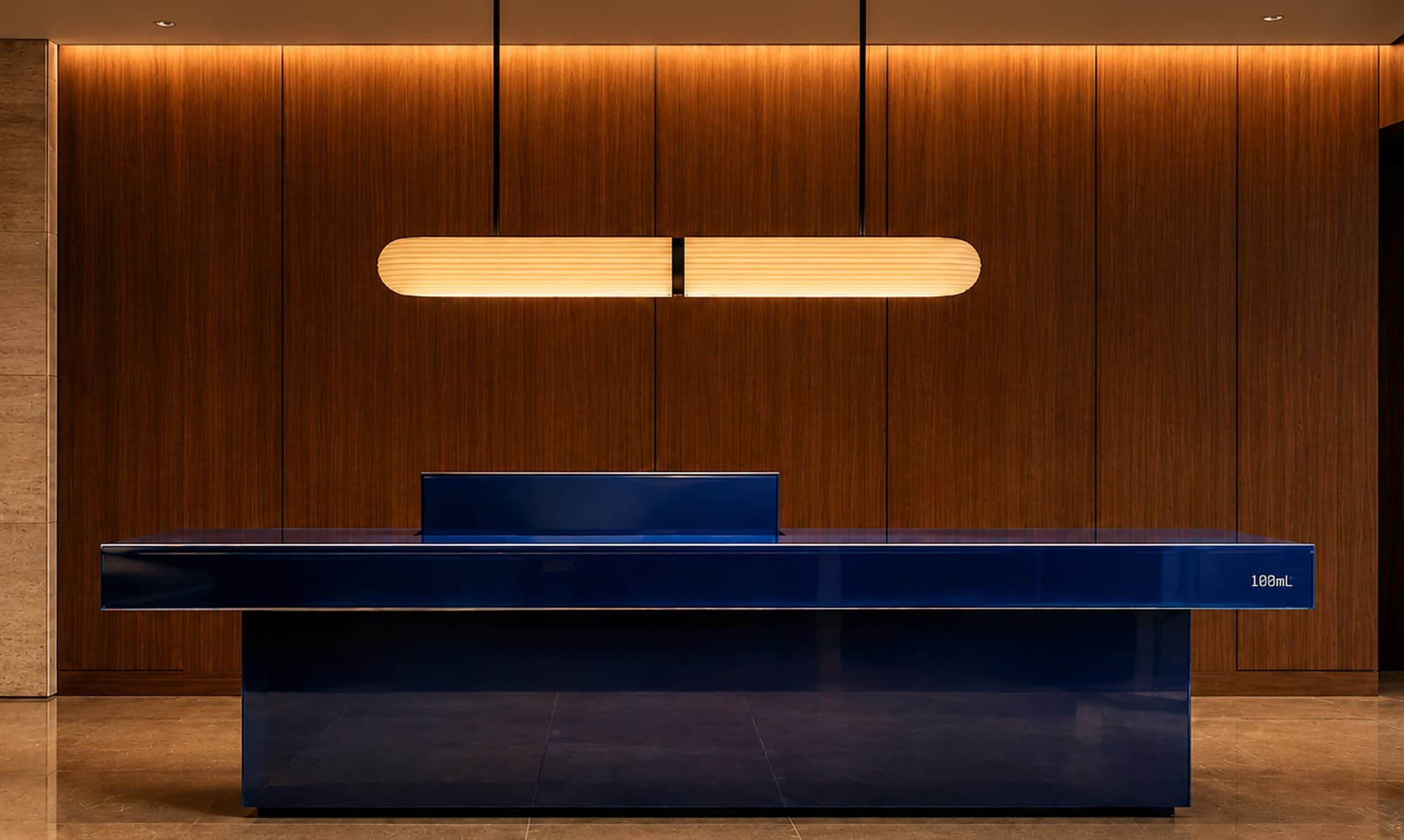 A cobalt lacquer reception desk beneath a linear pendant light in a walnut-panelled hotel lobby